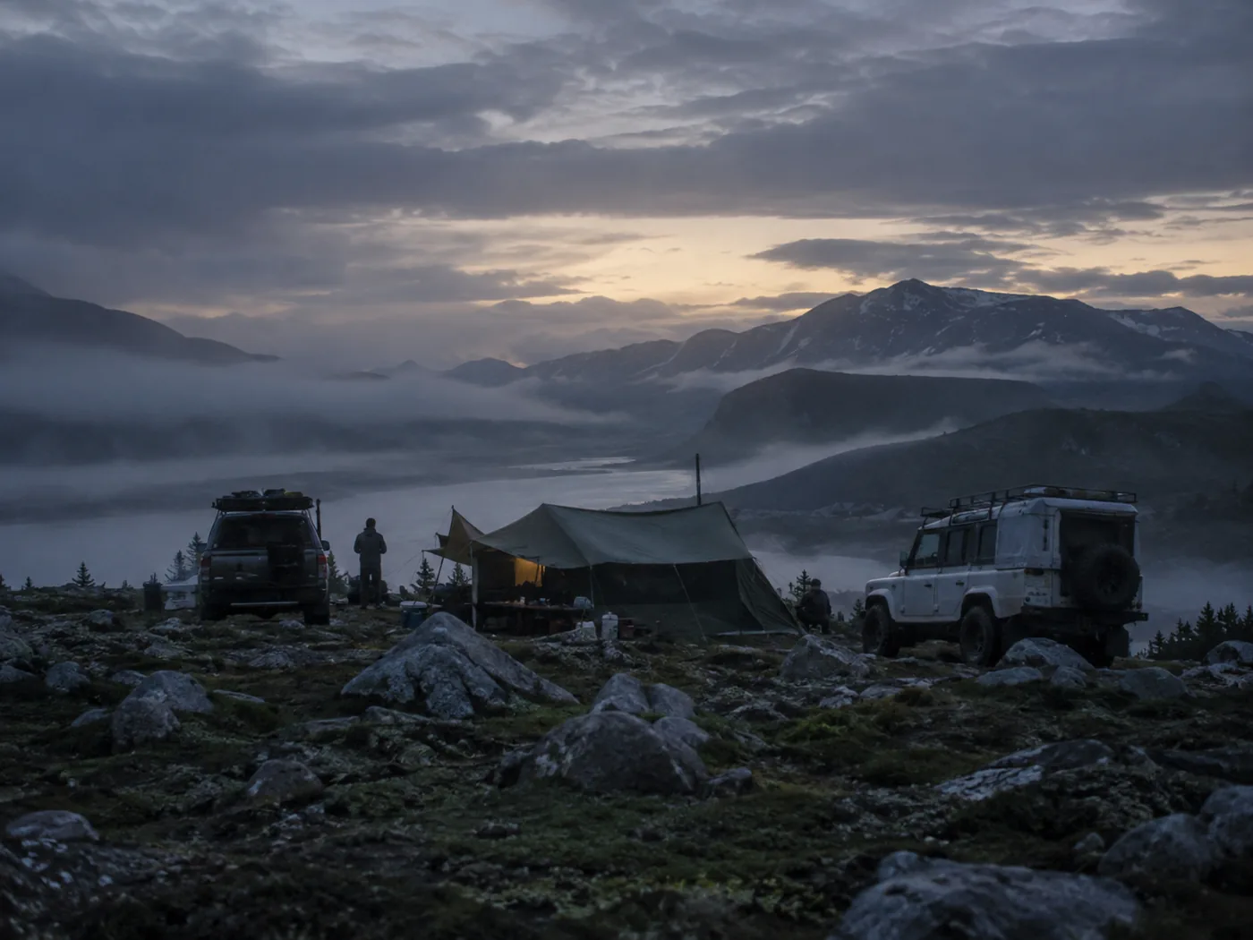 Mountain camp with vehicles and tents above the cloud line
